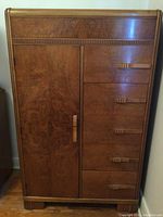 Full front view of wooden storage cabinet with five drawers on the right and one door on the left, showing carved handles and wood grain.