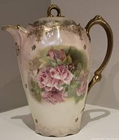 Front angle view of pink and white hand painted porcelain coffee pot with pink floral decoration, gold accents on spout and handle.