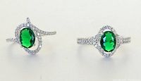 Top view of two costume rings showing oval green stones and clear stones on silver-tone bands.