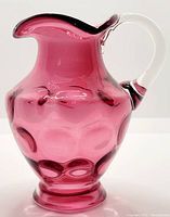 Front side view of cranberry glass pitcher showing coin dot design and clear handle.