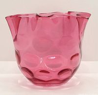 Front view of the cranberry glass bowl showing the ribbed coin dot textured pattern and smooth ruffle edge top.