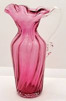 Full side view of the cranberry glass pitcher showing its swirl pattern and ruffled flared top edge.