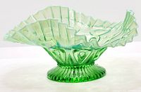 Side view of green to opalescent pedestal glass dish showing ruffled edge and raised beaded design.