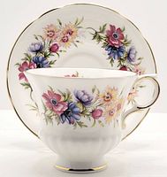 Front view of Paragon Flower Festival footed tea cup positioned in front of matching saucer showing floral design and gold trim