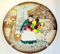 Full front view of Royal Doulton 'The Old Balloon Seller' collector plate showing seated elderly woman holding multicolored balloons in front of The London Pavilion building, with basket and pigeon at feet.
