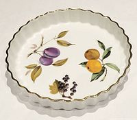 Overhead photo showing the round quiche dish with scalloped edge and painted fruit design inside, including plums, apricots, and blackberries with leaves.