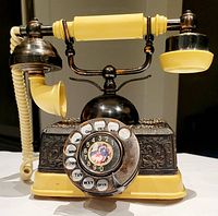 Front view of vintage European style rotary dial desk phone showing the rotary dial with lettered numbers and decorative floral metal body.