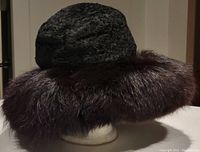 Side angle image showing the black textured top of the hat and full brown faux fur brim in good condition on mannequin stand.
