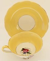 Photo of the yellow bone china saucer with scalloped edges and gold trim, showing front view.