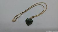 Full view of 18k yellow gold chain with heart-shaped green stone pendant laid flat