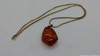 Full view of gold chain with amber pendant on white background