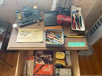Complete overview of calligraphy supplies laid on wooden table showing boxed ink bottles, pens, nib tips, stone ink desk set, booklet, and ink cartridges.