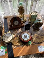 Full lot of vintage clocks, barometers, and thermometer on a table with sunlight and lace curtains in background