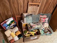 Overview of lot showing multiple cardboard and plastic boxes filled with yarn balls, embroidery thread, and supplies, with embroidery hoops leaning against the wall.