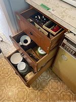 Photo of kitchen drawers showing various cutlery and utensils organized inside, along with ceramic casserole dishes.