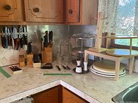 Wide view of kitchen counter with all items from the lot including glass canisters, teacup holder, lazy susans, utensils and salt and pepper shakers.