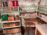 Several shelves filled with mason jars and glass storage jars mostly in branded boxes and some loose jars. Shelves and basement concrete wall visible.