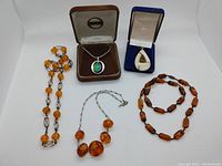 Overall view of two pendants in boxes and three amber necklaces on white background