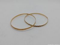Two gold bangles overlapping on white background, showing both finishes and shape