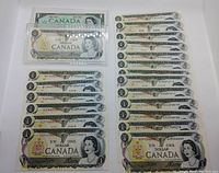 Top-down image showing 21 uncirculated Canadian 1 dollar bills. 20 bills stacked together, with one in a plastic protective case. One 1967 Centennial bill also in a plastic case visible.