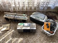 Photo showing multiple vintage electronic devices on carpet: Sharp stereo radio cassette recorder QT-77CW, Sony boombox, smaller radios, headphones and cables.