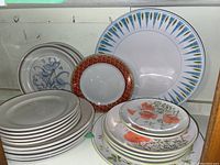 Display of set of vintage plates with different designs, varying sizes and colors, arranged on shelf.