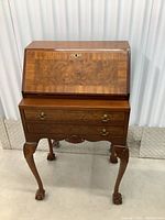 Front view of desk with closed fall front, two drawers, brass hardware, carved apron and cabriole legs