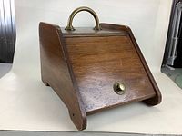 Angled side view showing solid wood construction, brass handle on top, and slant front panel with brass knob