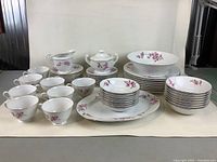 Full view of all pieces in the bone china dinnerware set including plates, bowls, cups, saucers, cream and sugar bowls, platter, and vegetable bowl on white background.