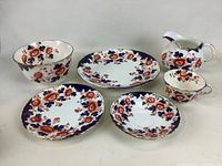 Full view of the entire Atlas fine china set, showing all 6 pieces arranged including the cake plate, dessert plate, bowl, jug, cup and saucer with Imari style floral design.