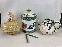 Photo showing walnut-shaped ceramic cookie jar with squirrel handle, colorful ceramic canister with fruit designs, ceramic teapot with green handle and fruit decoration, and metal nutcracker.