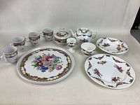 Full set showing small teapot, egg cup, small bowl, six mugs, and two plates with multi-color floral designs and gold accents.