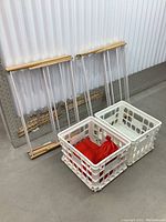 Two wooden and metal folding drying racks standing upright next to two white plastic storage bins, one containing a red air pump bag.