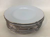 Stack of eight white salad plates with gold trim shown from top, highlighting the gold scalloped edge detail.