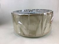 Photo shows the light fixture from a side angle highlighting the beige fabric shade wrapped in clear cellophane.