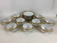 Full view of 9 handled soup bowls arranged in front of 10 matching saucers stacked