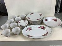 Full set including plates, saucers, cups, vegetable dish and platter arranged on white background