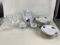 Dishes including soup plates, salad plates, teapot, cream, and sugar bowl with floral designs; and crystal glasses on a white background