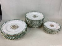 Full set of Royal Doulton plates consisting of three types arranged in stacks: side plates, salad/dessert plates, and lunch plates. Each has green and gold scalloped edge with gold floral pattern center.