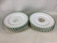 Stacked view of 16 Royal Doulton Camrose plates showing scalloped green and gold trimmed edges with floral center.