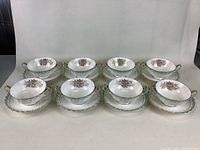 Front view of 8 fine bone china two-handle soup bowls and matching saucers, showing floral designs and gold trim