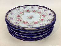 Stack of six vintage dessert plates showing blue rims, floral patterns, and gold trim