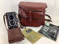 Camera inside its leather case with carrying bag and two instruction booklets laid out