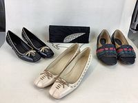 Photo of three pairs of women's shoes and a black clutch evening bag with shiny stones arranged on a white surface.
