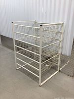 Front-right angled view of white metal wire frame storage rack with three wire mesh drawers, visible signs of wear on frame.