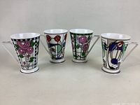 Four bone china mugs displayed in a row, showing colorful floral and geometric designs with footed bases.