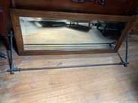 Full view of rectangular beveled mirror with wooden frame and metal bracket support on wooden floor.