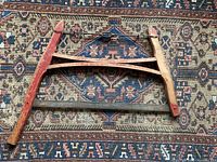 Full view of antique wooden frame hand saw laying flat on patterned rug, showing entire triangular red-painted wooden frame and metal blade.