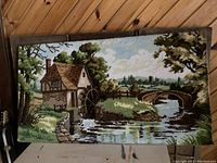 Full view of the large textile carpet wall hanging depicting a British rural landscape with a watermill, a bridge, and water reflections hung on a wooden paneled wall.