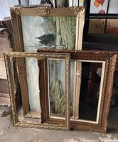 Three wooden picture frames stacked with one containing a landscape painting showing the size and style contrast between frames.
